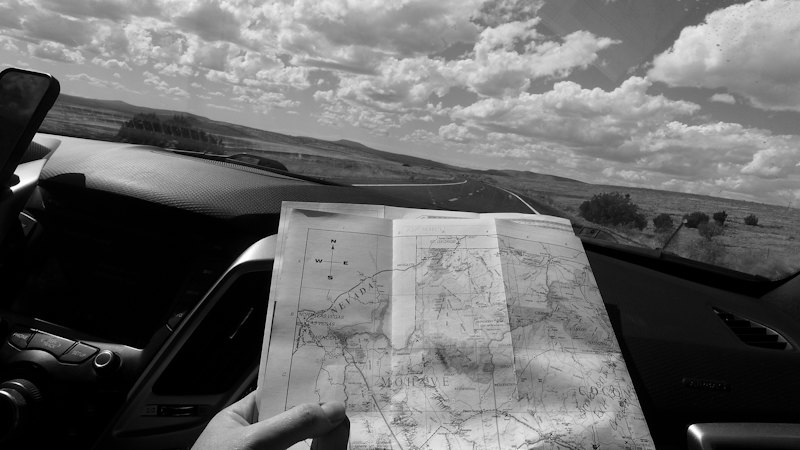 A hand holding up a paper map inside a car, the landscape beyond the windscreen
