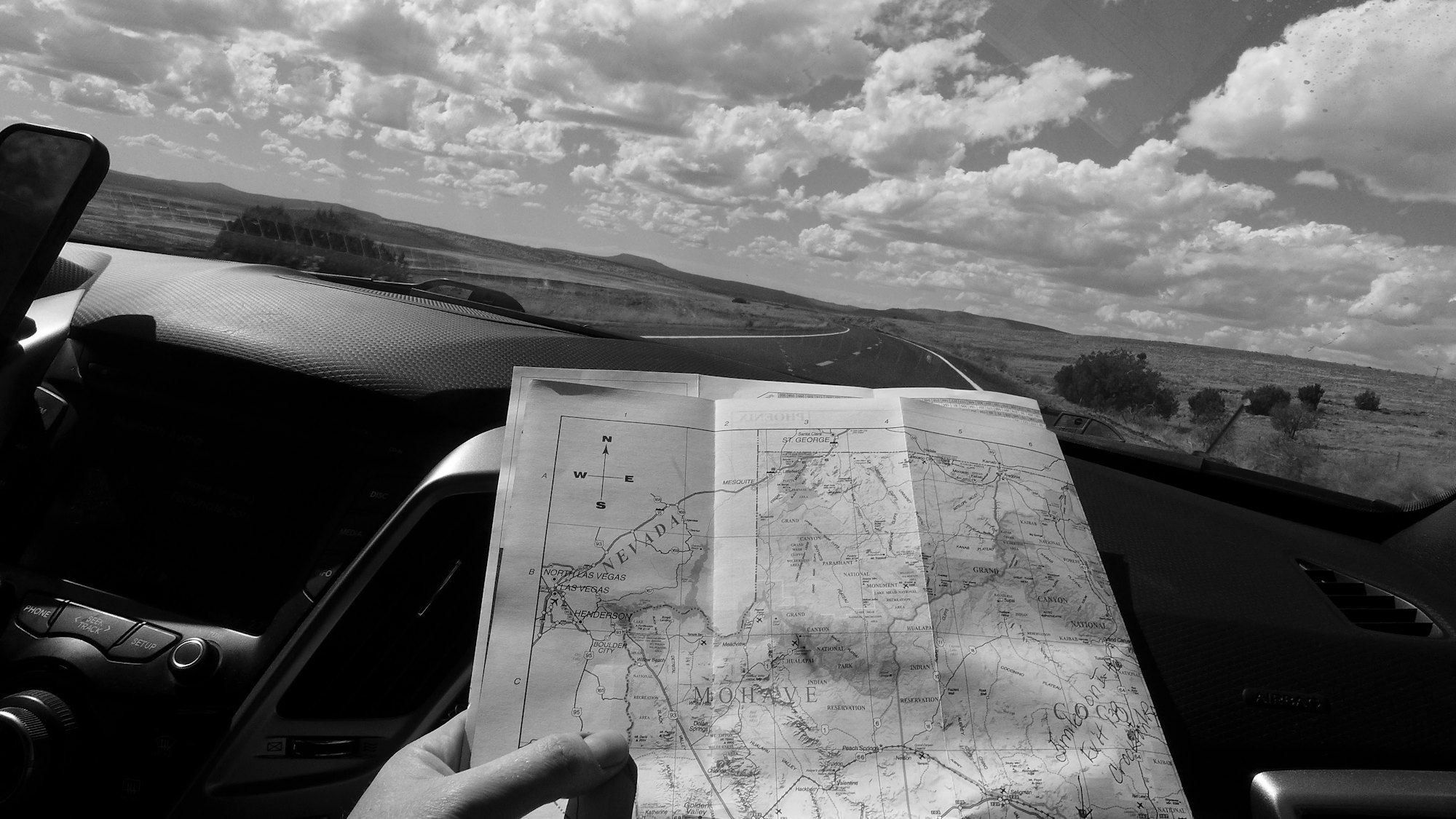 A hand holding up a paper map inside a car, the landscape beyond the windscreen