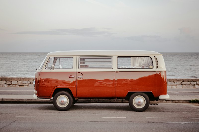 An orange and white VW bus parked on a seafront road
