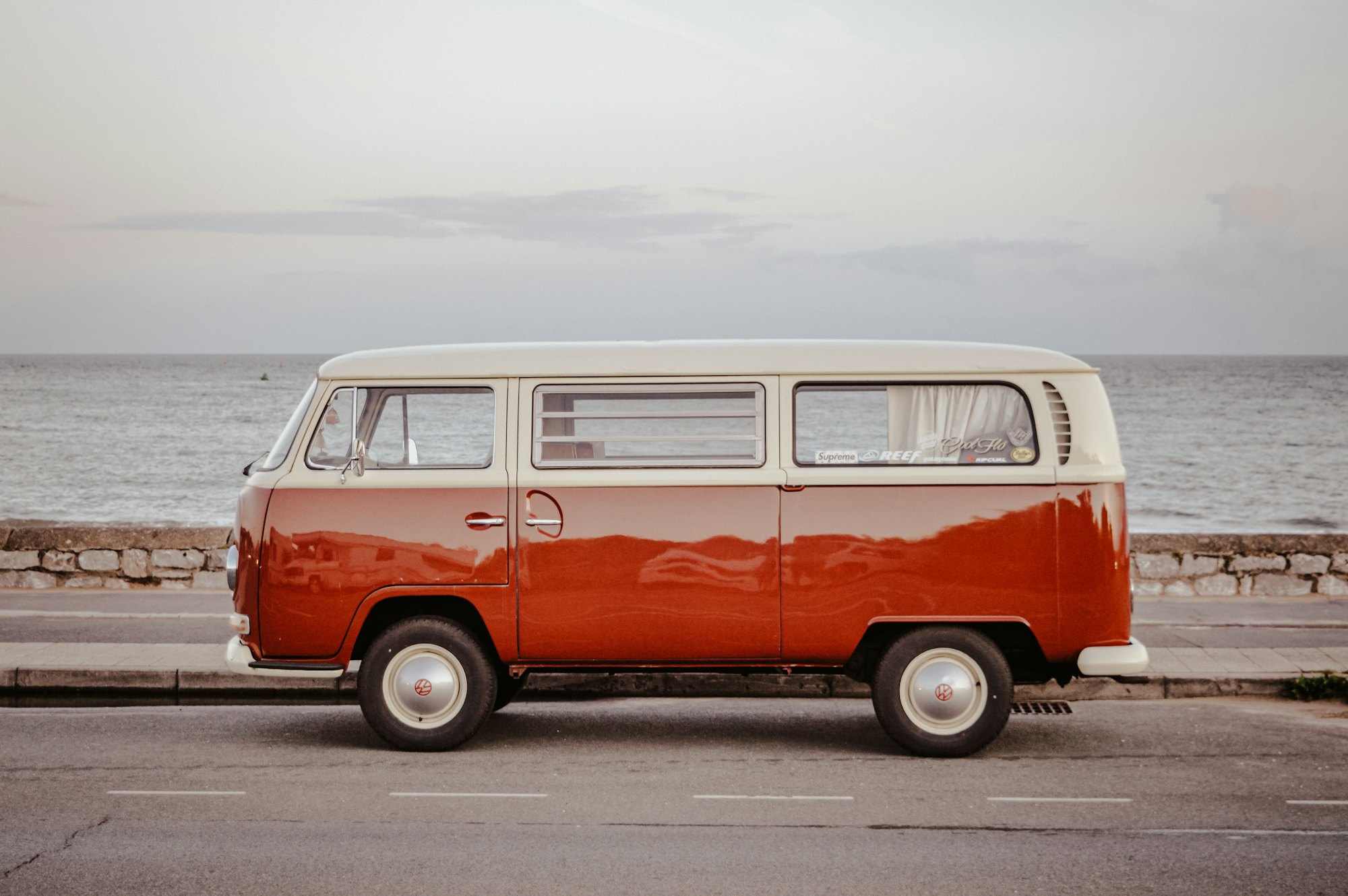 An orange and white VW bus parked on a seafront road