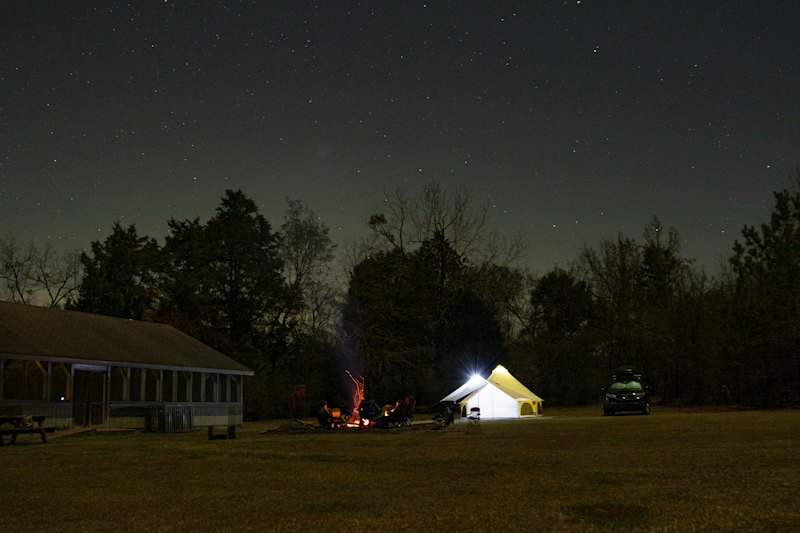 A tent and a small fire in a field at night