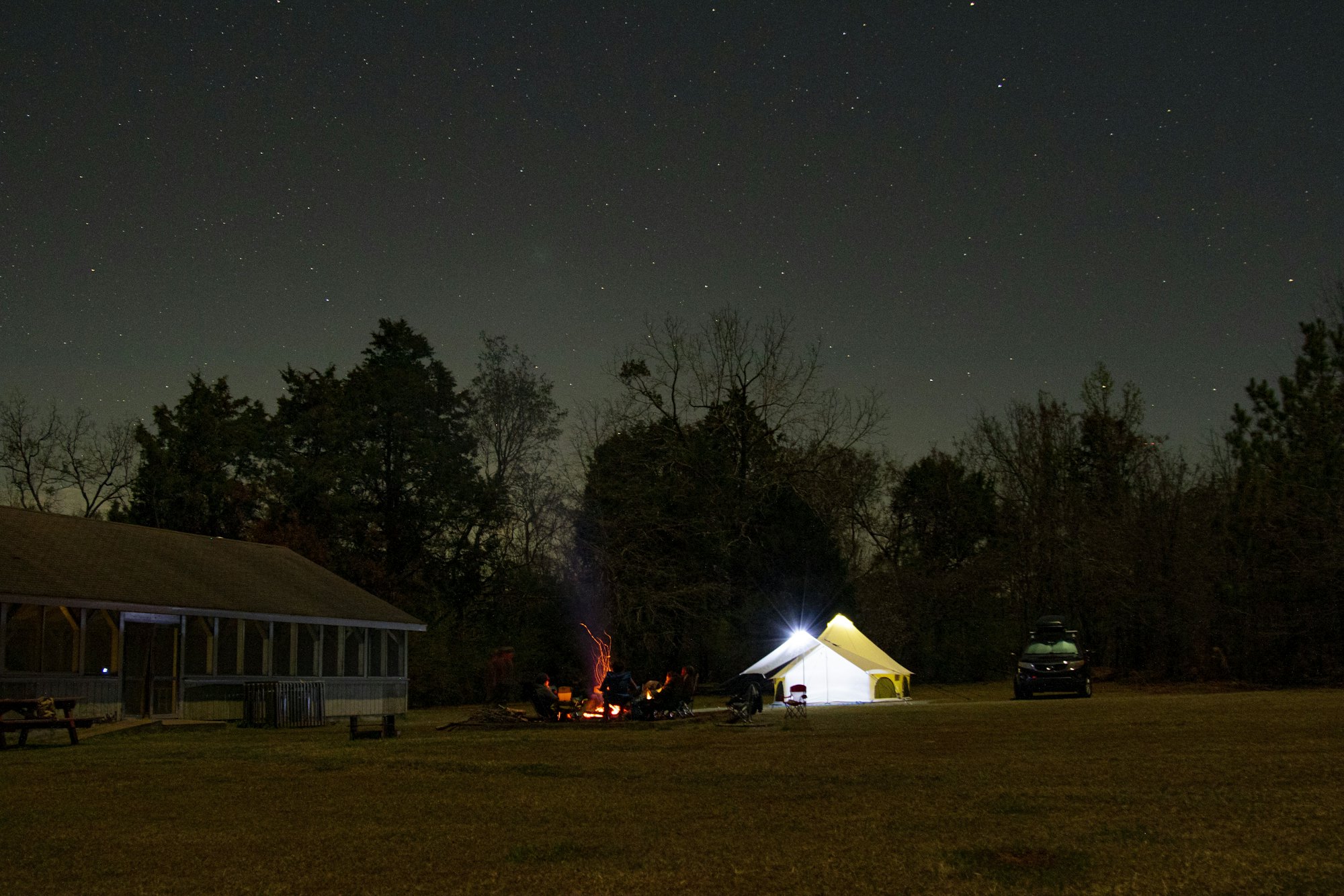 A tent and a small fire in a field at night